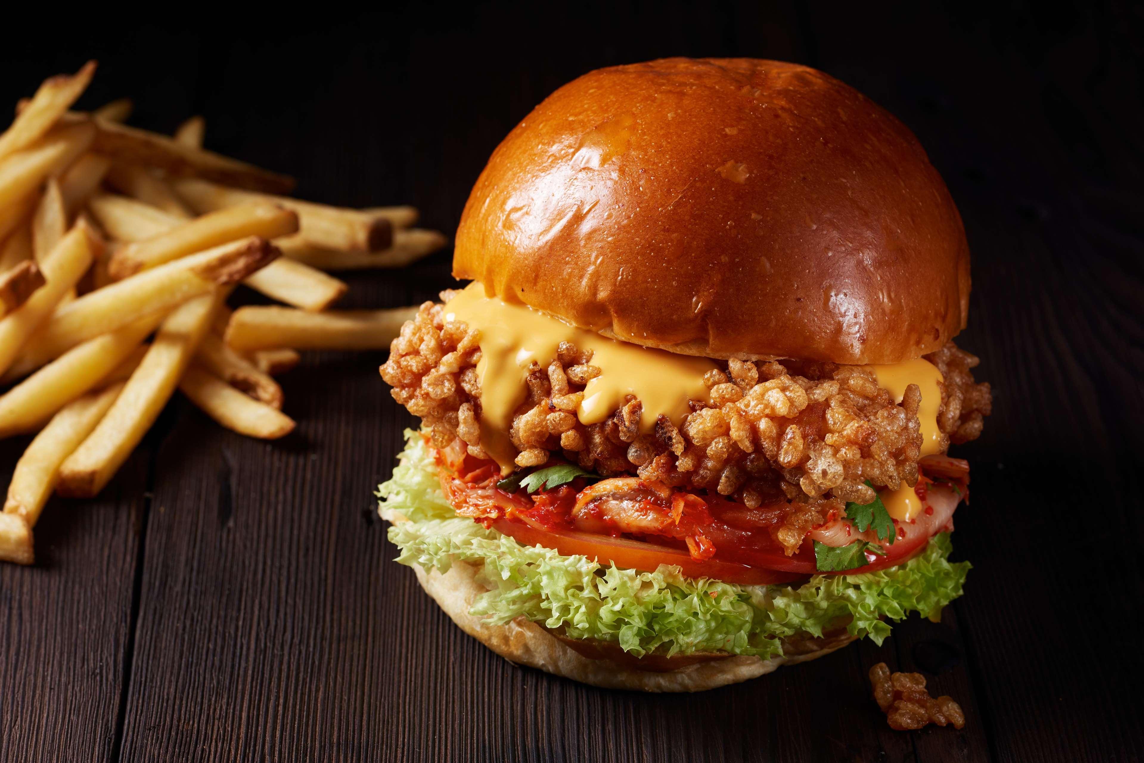 Hotel Atlantis, The Palm Dubai Esterno foto The photo shows a delicious-looking burger set against a dark wooden background. The burger features a glossy, toasted brioche bun on top and bottom. Inside, there is a crispy, fried chicken patty coated in crunchy bits, topped with melted cheddar ch