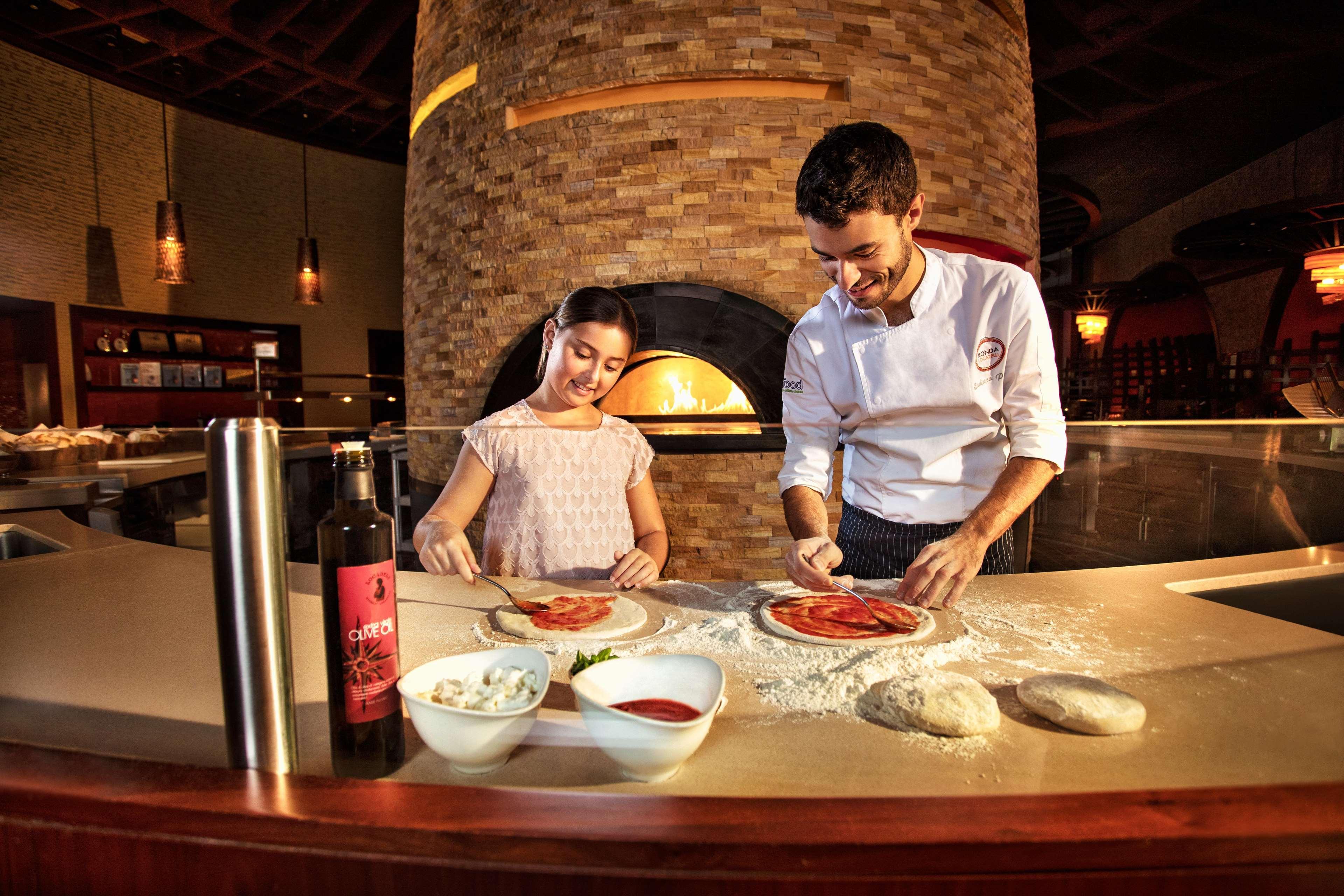 Hotel Atlantis, The Palm Dubai Esterno foto The photo shows a chef and a young girl working together in a kitchen setting. They are engaged in making pizza, with dough and various ingredients spread out on a counter. The girl is applying sauce or toppings to a pizza base while the chef, who ap
